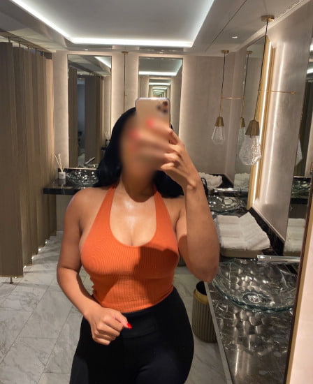 Curvy ebony girl in an orange top taking a selfie
